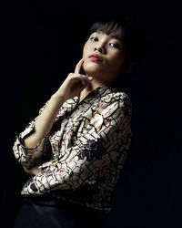 Portrait of young woman standing against black background