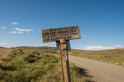 Hand carved letters on wooden road sign along rural dirt road against sky