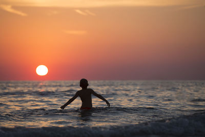 Full length of man on sea against sky during sunset