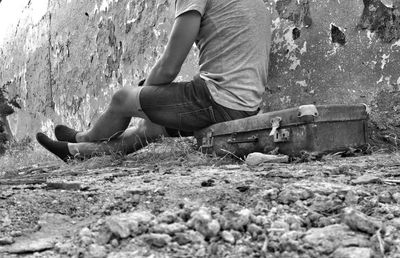 Low section of man sitting by wall on suitcase