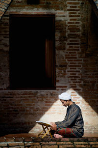 Side view of a man sitting on brick wall