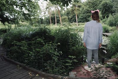 Rear view of girl standing by trees in forest