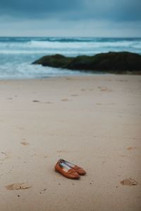 Close-up of shoes on beach against sky