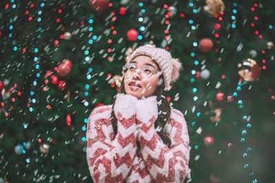 Portrait of woman standing against illuminated christmas tree