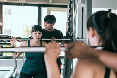 Man helping woman in lifting barbell at gym