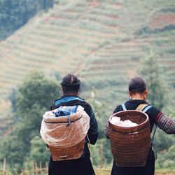 Rear view of women with wicker baskets on field by mountain