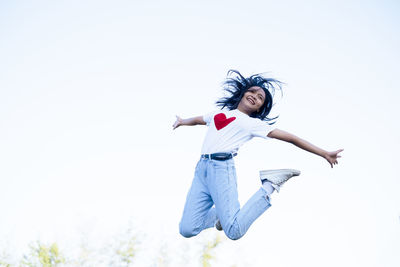 Full length of a young woman jumping against clear sky