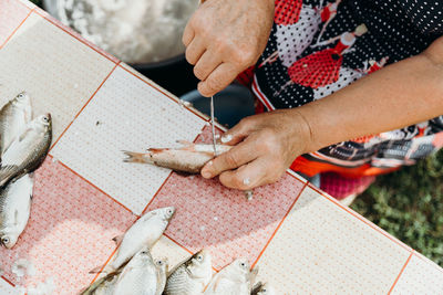 An elderly woman cleans fish from scales at the table.