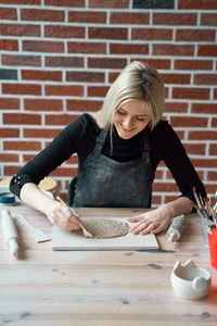 Midsection of woman holding ice cream on table against brick wall