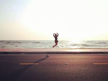 Woman jumping over footpath by road against sky