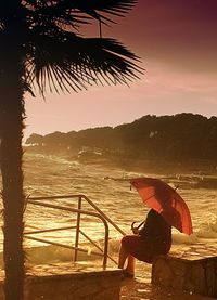 Silhouette woman sitting on beach against sky during sunset