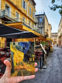 Person holding umbrella on street by buildings in city