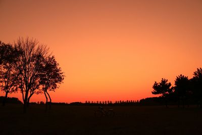 Silhouette trees on field against orange sky