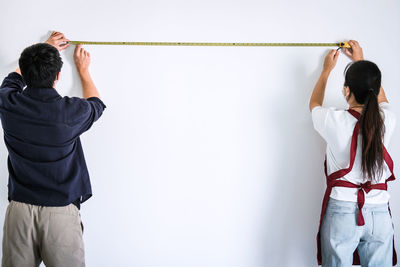 Rear view of people measuring white wall