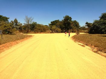 People walking on road against clear blue sky