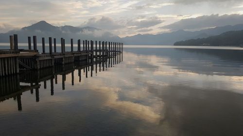 Wooden posts in lake against sky during sunset