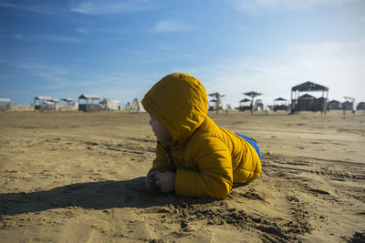 Boy lying on sand at beach against sky