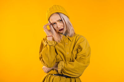 Portrait of young woman gesturing against yellow background