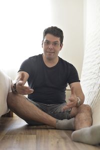 Portrait of young man sitting on hardwood floor