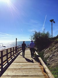 Rear view of people walking on pier over sea against sky