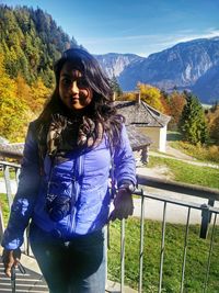 Portrait of young woman standing against railing and mountains