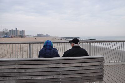 Rear view of couple sitting on sea shore against sky