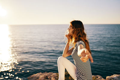 Woman sitting by sea against sky