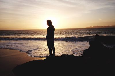 Silhouette man standing on beach against sky during sunset