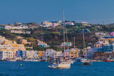 Sailboats in sea by townscape against sky