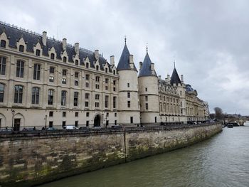 Buildings by river against cloudy sky