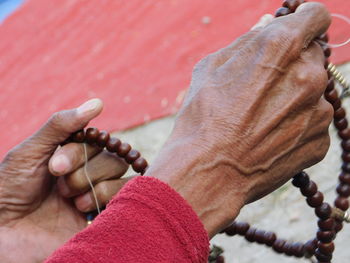 Close-up of wrinkled hands holding bead necklace