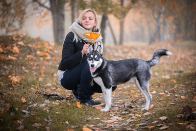 A young woman trains her siberian husky dog in a park covered with autumn leaves