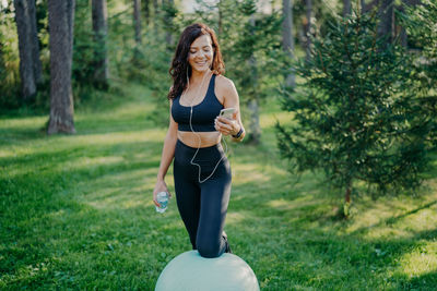 Smiling woman using smart phone while standing by fitness ball in park