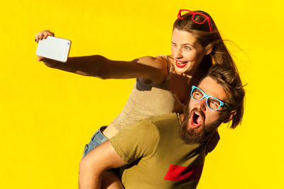 Portrait of smiling young woman using mobile phone against yellow background