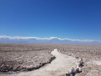 Scenic view of path in desert against blue sky