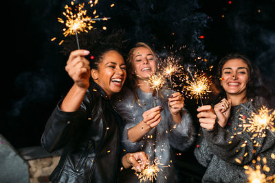 Cheerful female friends holding illuminated sparklers
