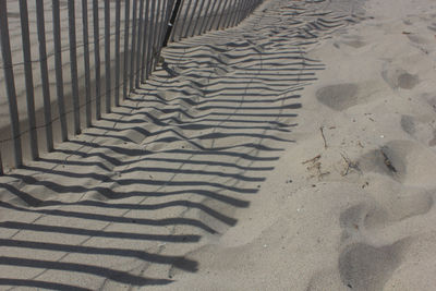 Shadow of fence on sand during sunny day