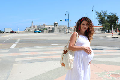 Portrait of young pregnant woman walking in old havana on road against sky