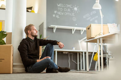 Thoughtful young male entrepreneur sitting on floor at creative office