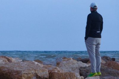 Man standing on rock by sea against sky