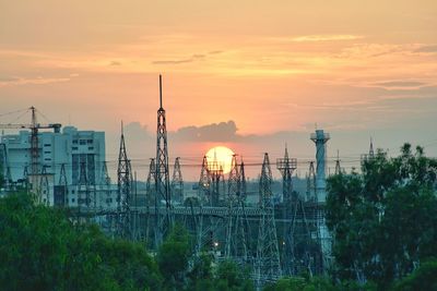 View of electricity pylons in city against sky during sunset