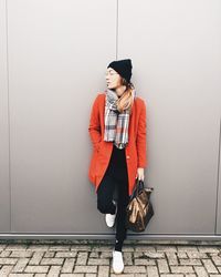 Young woman using mobile phone while standing against wall