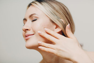 Close-up of woman applying face mask against colored background