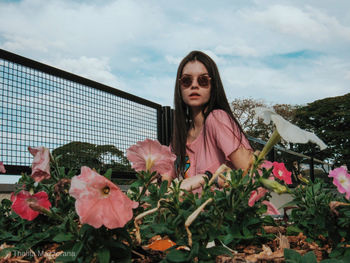 Portrait of beautiful young woman standing by flowering plants against sky