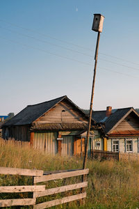 Old wooden house on field by buildings against sky