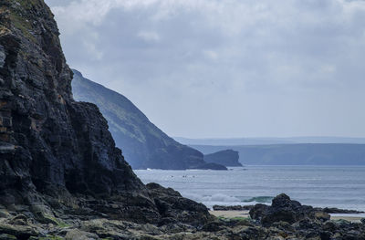 Cliff by sea against cloudy sky