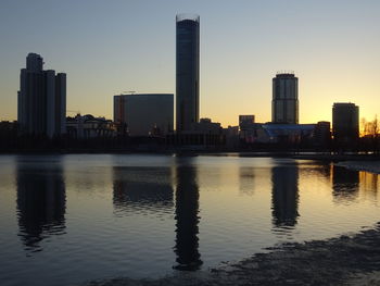 Buildings by river against sky during sunset