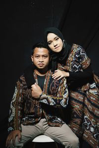 Portrait of young couple sitting against black background