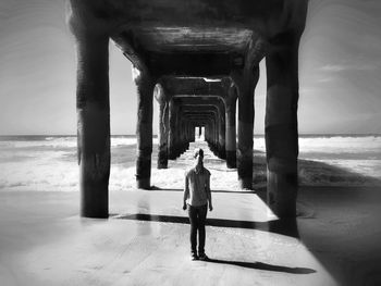 Rear view of girl standing below pier at beach