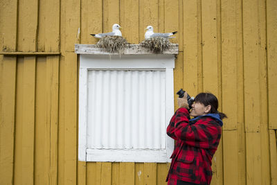 Woman photographing birds in nest over window